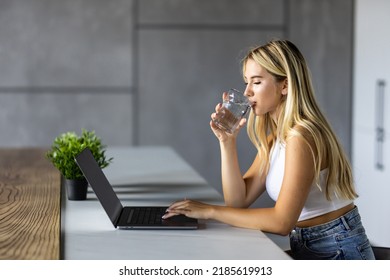 Shot of beautiful woman working with laptop while drinking glass of water on desk in office at home. - Powered by Shutterstock