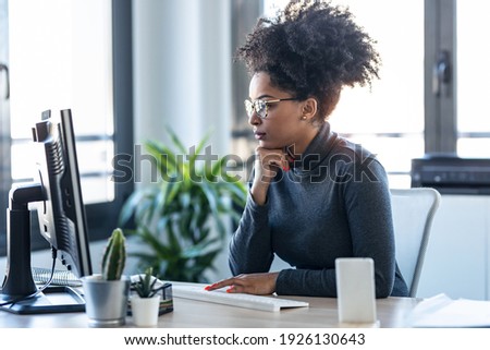Shot of beautiful young afro business woman working while making video call with computer sitting in the office.