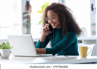 Shot Of Beautiful Young Business Woman Talking On Mobile Phone While Working With Her Laptop In The Office.