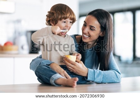 Shot of beautiful young mother giving food to her son while having fun in the kitchen at home.