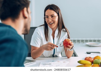 Shot of beautiful young nutritionist woman explaining to her patient the diet he should follow to lose weight in the consultation.