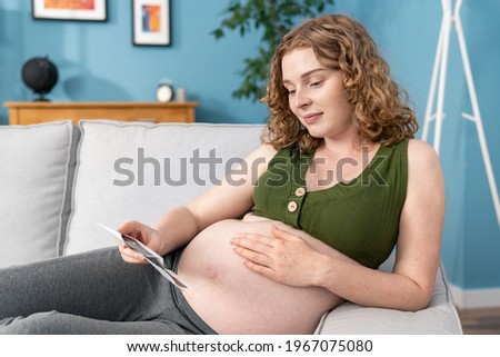 Shot of beautiful young pregnant woman looking ultrasound pictures of her baby while lying on bed.