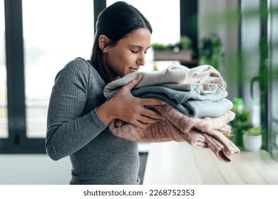 Shot of beautiful young woman holding and smelling clean clothes at home. - Shutterstock ID 2268752353