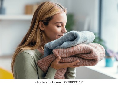 Shot of beautiful young woman holding and smelling clean clothes at home.