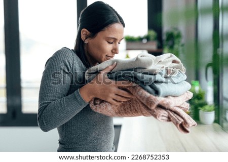 Shot of beautiful young woman holding and smelling clean clothes at home.