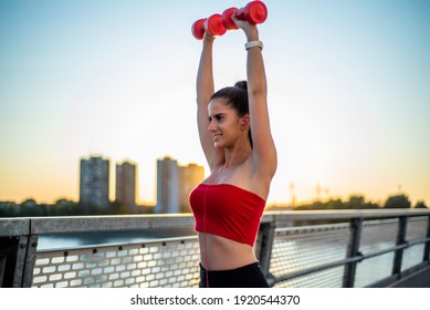 Shot Of A Beautiful Young Woman Lifting Weights During A Outside Training In The Morning