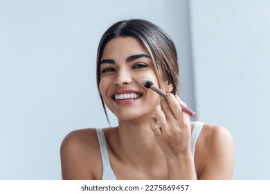 Shot of beautiful young woman making make-up near mirror in the bathroom.