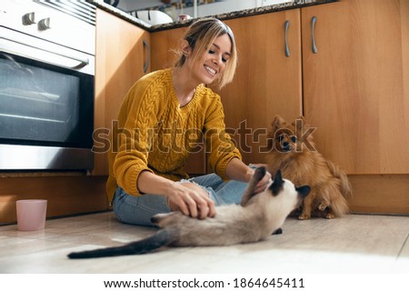 Shot of beautiful young woman playing with her cute lovely animals sitting on the floor in the kitchen at home.
