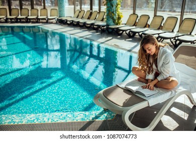 Shot of a beautiful young woman reading by the pool
