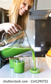 Shot Of Beautiful Young Woman Serving Detox Green Juice Into Glasses At Home.