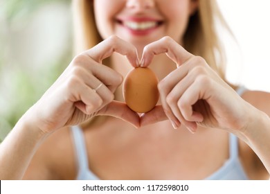 Shot of beautiful young woman showing brown chicken egg with hands in a heart shape at home. - Powered by Shutterstock