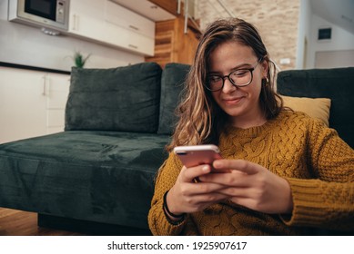 Shot of a beautiful young woman using her cellphone while relaxing on a couch at home