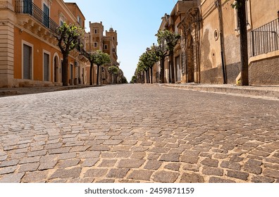 Shot from below a cobbled stone street, without people, lined with low buildings and trees, under the afternoon sun of a typical Sicilian village. - Powered by Shutterstock