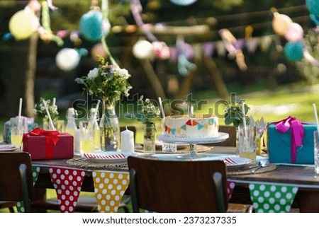Shot of the birthday table with colorful decorations, birthday cake, and gifts. Inspiration for simple, tasteful birthday decoration for a garden party.