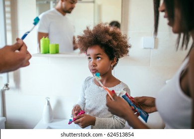 Shot Of Black Family Teaching Their Daughter To Brush Her Teeth In The Bathroom.