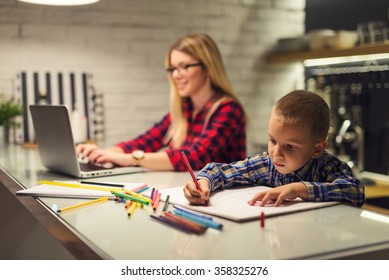 Shot of a boy drawing while his mother is working on a computer. - Powered by Shutterstock