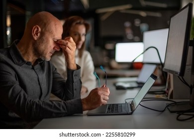 Shot of a businessman looking exhausted while sitting at his desk in the office in late evening. Tired professional man having headache. - Shutterstock ID 2255810299