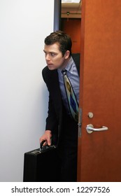 A Shot Of Businessman Peaking His Head Out Of A Door To See If He Can Sneak Out The Office.