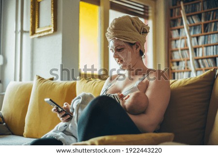 Shot of a busy working mother breastfeeding her baby boy while wearing spa face mask and a towel on her head