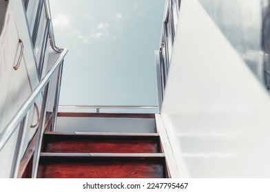 A shot captured from the lower deck when climbing a wooden stairway and shiny metallic railings leading to the upper deck of a white sailing yacht; on a warm sunny clear sky day in the Maldives island
