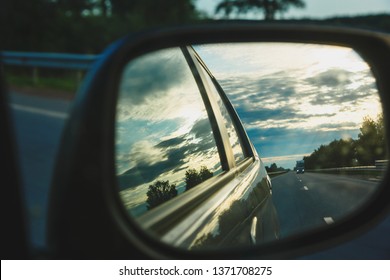 Shot Of Car Rare View Mirror Reflects  Sunset With White Clouds And Road Ahead As Background