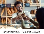 Shot of cheerful seller giving fresh loaf of bread to smiling woman in the pastry shop.