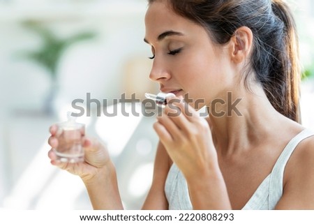 Shot of a cheerful woman girl holding a bottle of essential oil while testing it sitting on a couch at home.