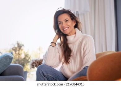 Shot of cheerful woman relaxing on the sofa at the armchair. Attractive woman wearing casual clothes while sitting on the chair.