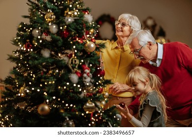A shot of a Christmas tree being decorated with Christmas decoration by a little girl and her grandparents - Powered by Shutterstock