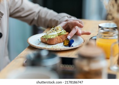 Shot of close-up of woman hands holding eggs benedict on toast with advocado for breakfast on the healthy coffee shop terrace. - Powered by Shutterstock