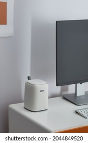 Shot Of A Computer Desk With A Monitor, Keyboard And White Desktop Trash Can. There Is A Picture On The Light Wall. White Trash Can, Gray And Black Monitor, Keybord Are Staying On The Desk.