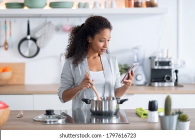 Shot of confident young african american woman cooking healthy food while using her mobile phone in the kitchen at home. - Powered by Shutterstock