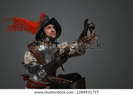Shot of conquistador with plumed helmet and plate armor holding broken epee.