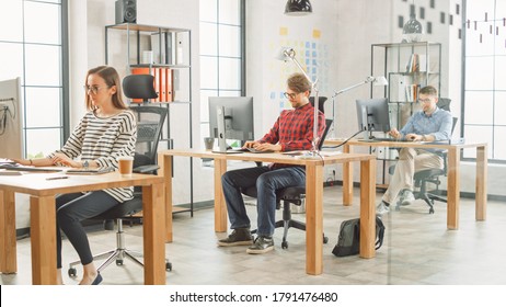 Shot Of Creative Agency Life. Female Colleague Works With Two Male Coworker Behind Desks. Creative Office Concept. They Work On Computers And Laptops.