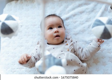 Shot of a cute baby girl is watching and playing with children's musical mobile toy at home.