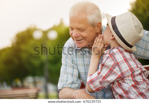 Shot of a cute little boy whispering something\
to his grandfather while resting together outdoors copyspace family\
communication relationships trust happiness love gossip children\
kids parenting
