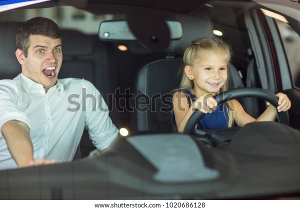 Shot of a cute little girl sittin in the car\
behind the steering wheel pretending to drive her father screaming\
looking terrified family playtime playful emotions danger safety\
driving insurance