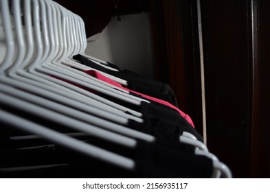 A Shot Of Dark Colored Clothes Hanging On White Hangers In A Dark Closet