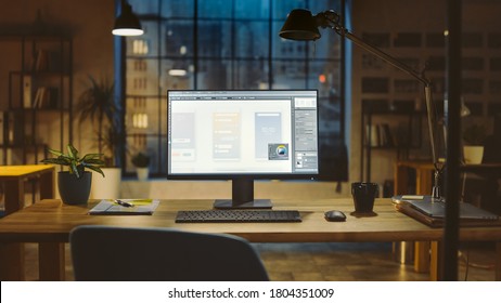 Shot Of A Desktop Computer In The Office Shows Screen With Mobile Phone Application Design, Software UI Development. In The Background Warm Evening Lighting And Open Space Studio With City Window View