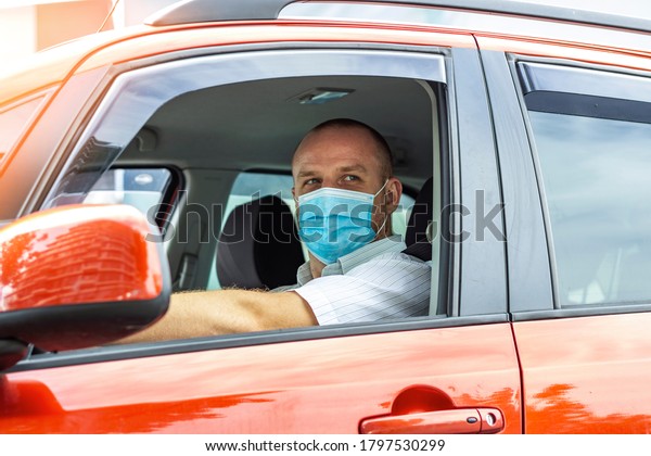 Shot of driver wearing protective medical mask. Young\
male driver inside car with protective face mask. Man driving car\
with a protection mask in the city. Adult man driving to work\
wearing face mask 
