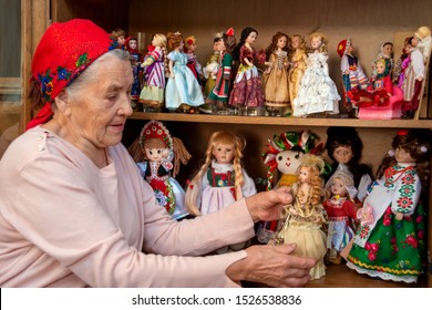 Shot Of An Elderly Asian Woman With A Bandaged Headscarf Looking At Dolls In Beautiful Dresses From Her Collection At Home.  Interesting Hobby For The Elderly