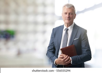 Shot of an elderly managing director with diary standing in conference room after business meeting. 