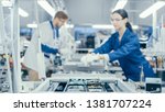 Shot of an Electronics Factory Workers Assembling Circuit Boards by Hand While it Stands on the Assembly Line. High Tech Factory Facility.
