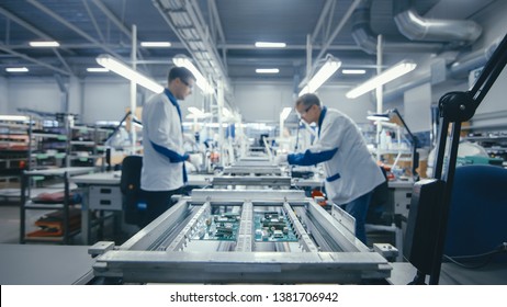 Shot Of An Electronics Factory Workers Assembling Circuit Boards By Hand While It Stands On The Assembly Line. High Tech Factory Facility.