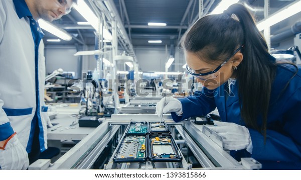 Shot of an Electronics Factory Workers\
Assembling Circuit Boards by Hand While it Stands on the Assembly\
Line. High Tech Factory\
Facility.