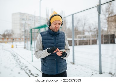 A shot emphasizing the movement and strength of a runner with headphones and smartphone, as he jogs through the winter terrain. showcasing the power and dedication of a dedicated runner. - Shutterstock ID 2256579883