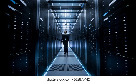 Shot of IT Engineer Walking Through Data Center Corridor with Rows of Rack Servers.