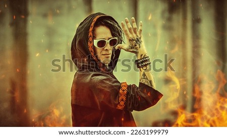 A shot of an expressive mature man with dreadlocks, tattoos and sunglasses in black clothes with ethnic ornaments poses on the backstreet. Rock and punk culture. 