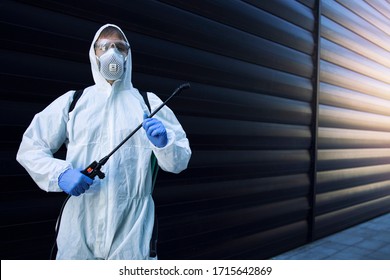 Shot of exterminator person in white chemical protection suit doing disinfection and pest control and spraying poison to kill insects and rodents. Successful pest control and extermination.