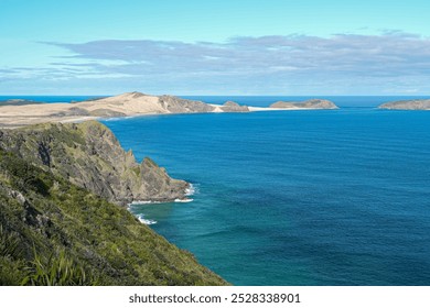 A shot of the famous coastal cliffs at Cape Reinga, where the Tasman Sea meets the Pacific Ocean. The iconic view captures the rugged landscape, bathed in sunlight under a bright blue sky. - Powered by Shutterstock